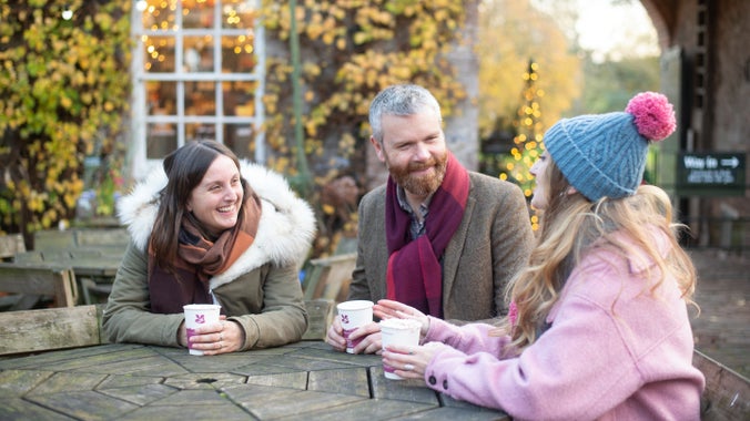 A group of friends sit around a table drinking hot drinks along the Christmas trail at Killerton, Devon